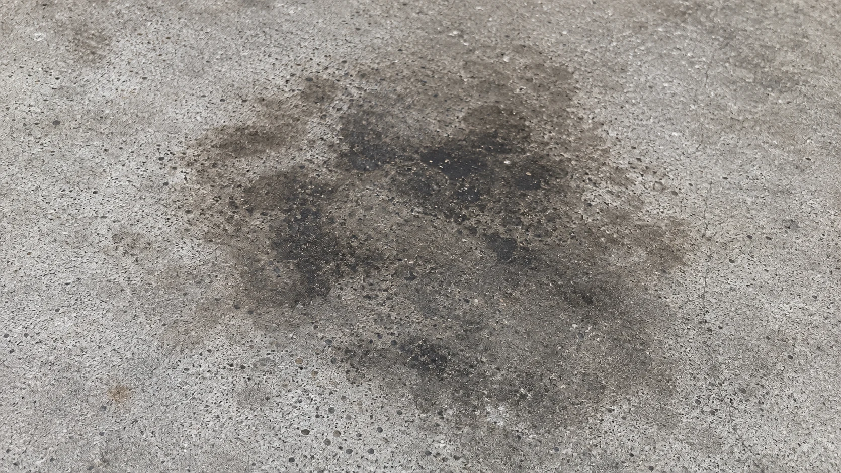 Dark oil and grease stain on a concrete driveway where a car parks